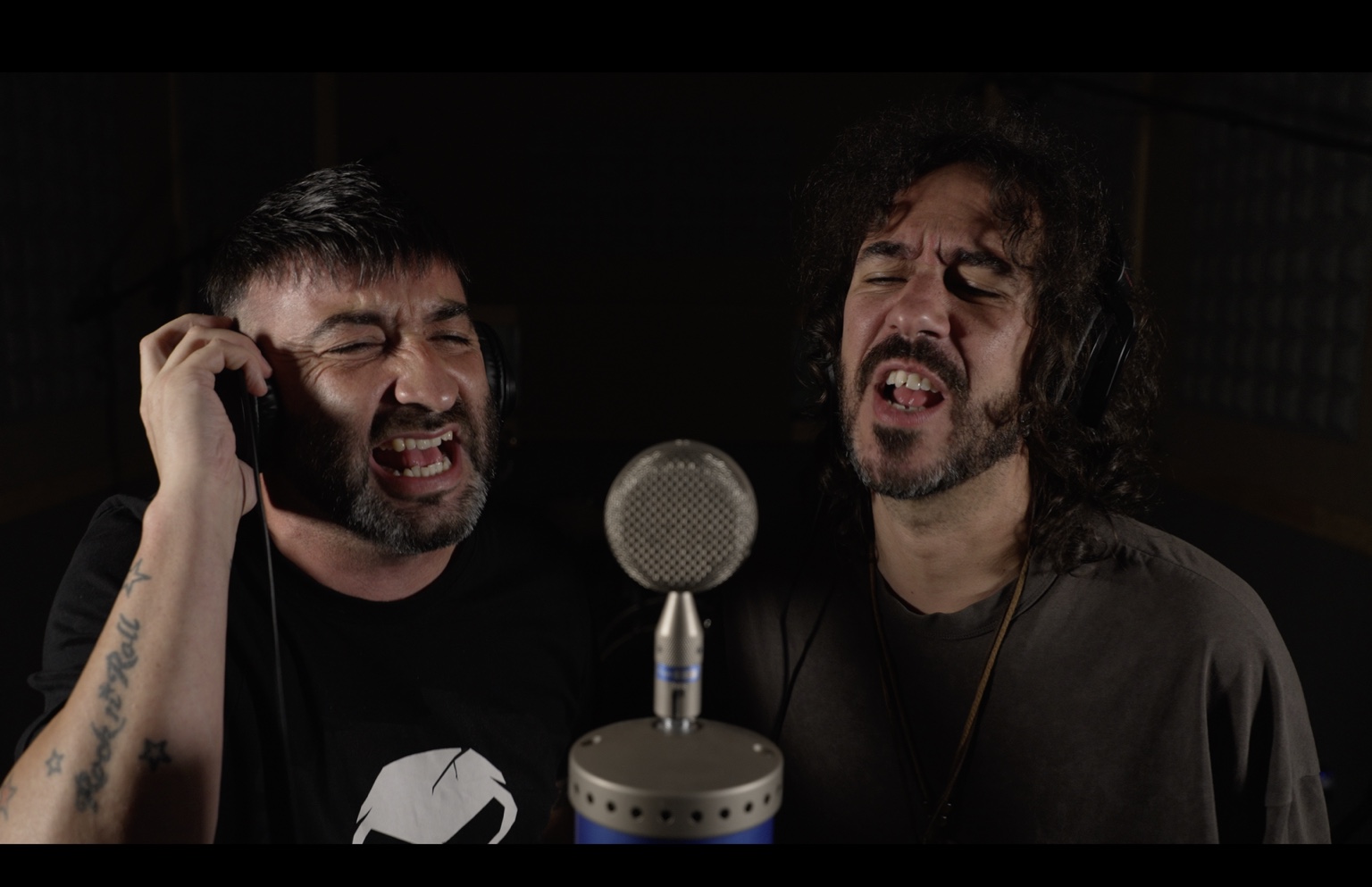 Dos cantantes compartiendo micrófono durante una grabación en el estudio
